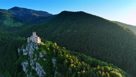 flying closer to the unapproachable rock with a castle on top. wooded tatra mountains at backdrop. aerial view