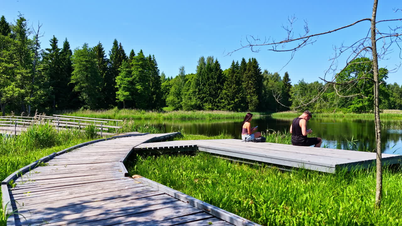 Two people relaxing on wooden path by lake in Kirkilai Lakes nature reserve