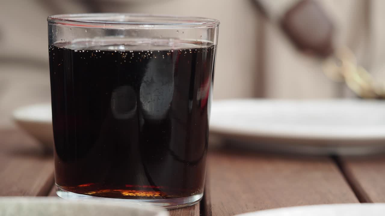 Rinfrescante bicchiere di Cola con bollicine su un tavolo di legno.