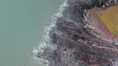 AERIAL:-Top-down-fly-along-jagged-rock-coastline,-Rhossili-Gower,-4k-Drone