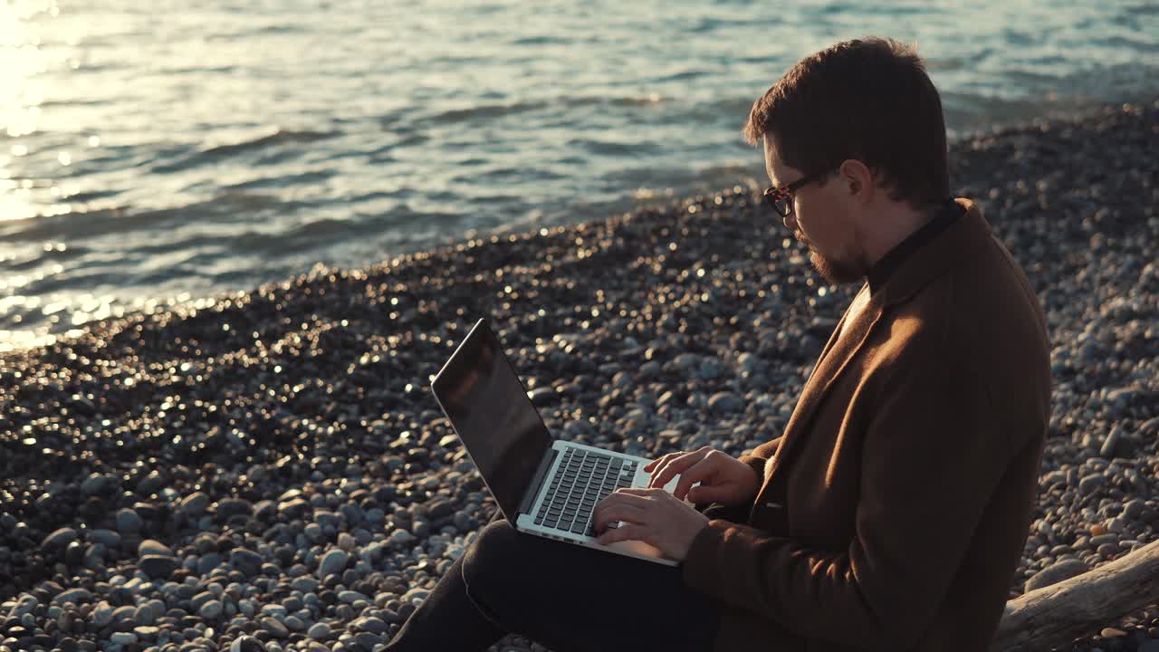 Man working on laptop on the beach at sunset