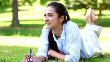 pretty girl lying on the grass writing on notepad