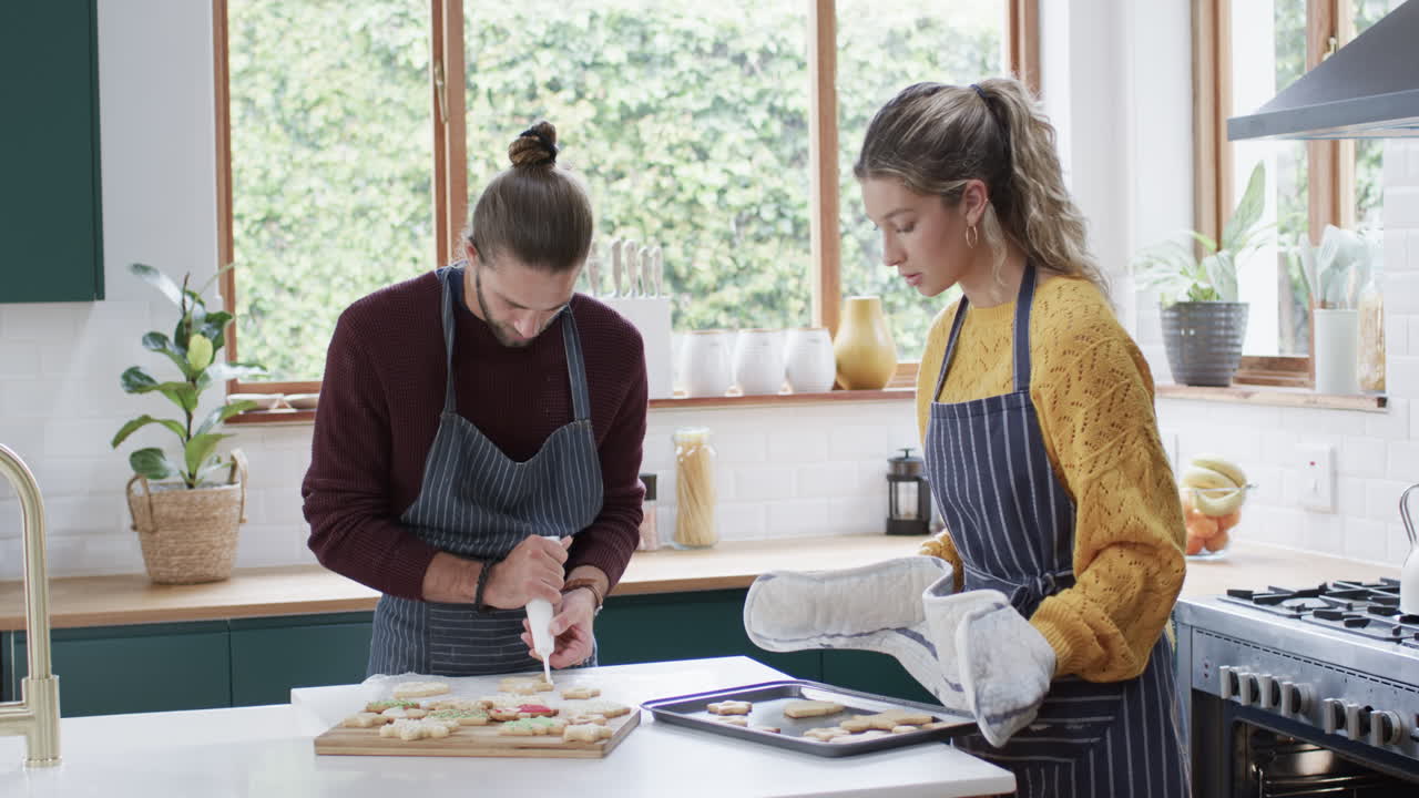 pareja feliz decorando galletas de navidad en la cocina en casa, en cámara lenta