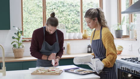 Happy-diverse-couple-decorating-christmas-cookies-in-kitchen-at-home,-in-slow-motion