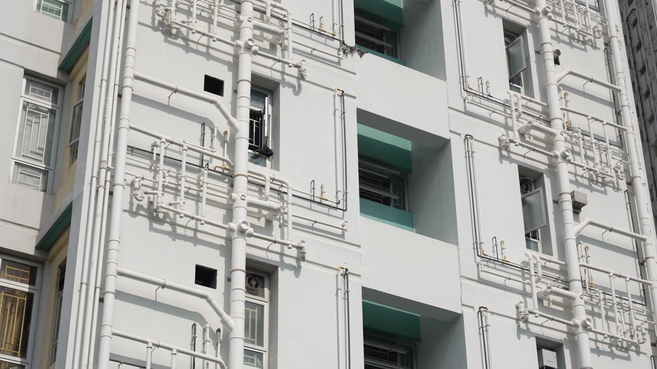 Vista della facciata esterna di un moderno edificio residenziale con pareti bianche e rete di tubazioni esterna.