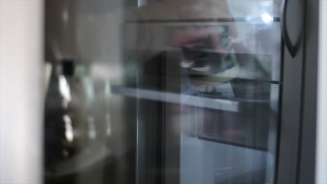 unrecognisable young man walks over to a refrigerator and stores a can of mayonnaise