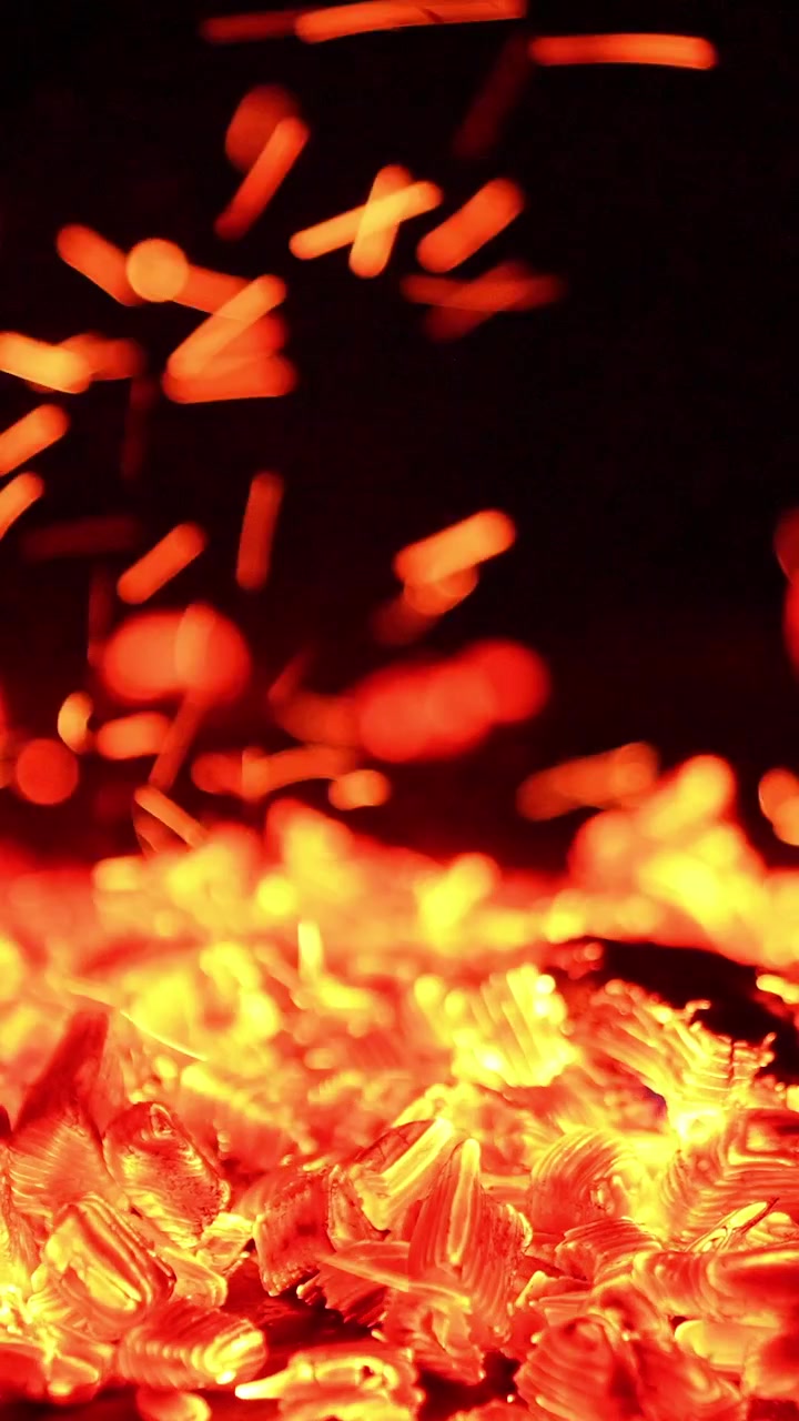 キャンプファイヤーの熱い熾火。燃える炭と舞い上がる小さな火花のクローズアップ。縦型動画