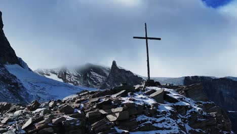 Close-up-Christian-Catholic-religious-Jesus-Christ-Cross-rocky-glacier-mountain-top-drone-aerial-Saas-Fee-Swiss-Alps-Switzerland-fall-autumn-sunny-blue-sky-mid-day-cloudy-layer-forward-circle