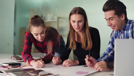 grupo de diseñadores de interiores preparando el proyecto juntos en la oficina. están haciendo bocetos y borradores pintando con lápices y regla. jóvenes hipsters discutiendo su nuevo proyecto