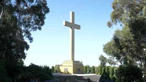 large remembrance cross in sunlight framed by tall trees either side