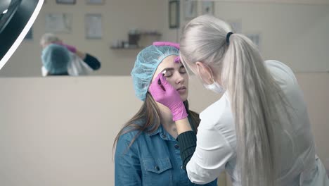 makeup master makes eyebrow tattooing to client in salon