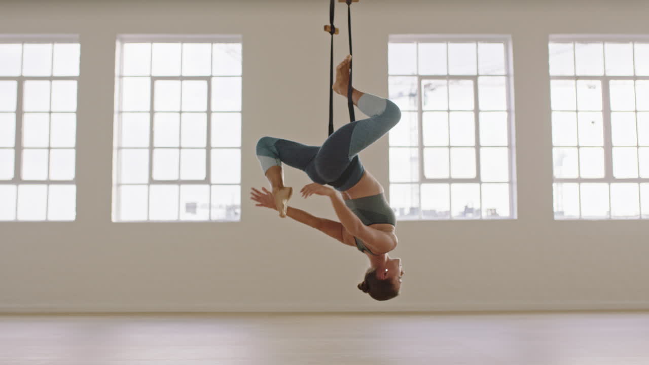 aerial yoga woman practicing bound one-legged king pigeon pose hanging upside down using hammock enjoying healthy fitness lifestyle exercising in studio training meditation at sunrise