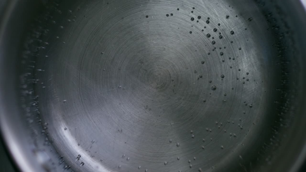 A close-up top view of water boiling in a metal pot on the stove