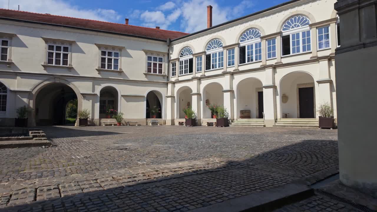 Carrellata in avanti verso il cortile interno del Castello di Sárospatak, in Ungheria, che mette in risalto la sua architettura tardo-rinascimentale, gli archi in pietra, i sentieri acciottolati e l'eleganza storica in autunno