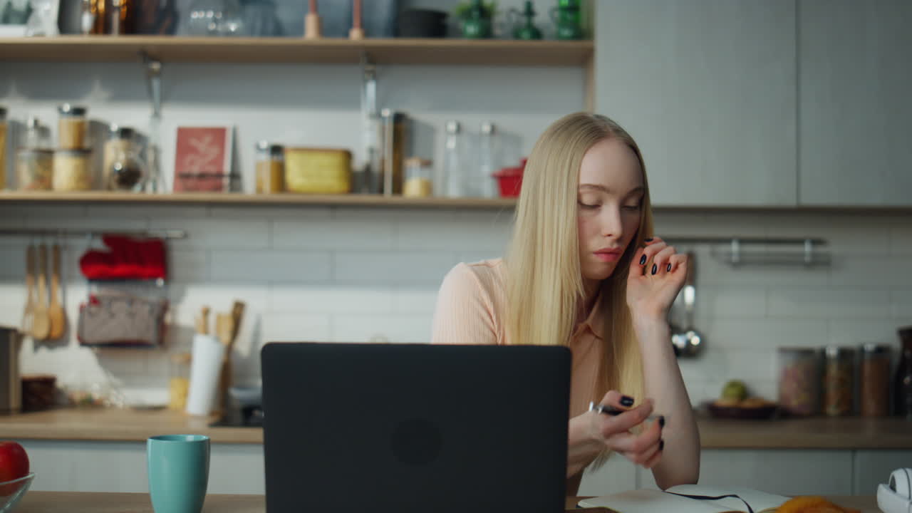Nærbillede af kvinde, der ser et uddannelseswebinar på bærbar computer i køkkenet.