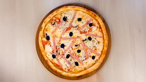 pizza with ham and cheese on wooden board on the table. close-up view.