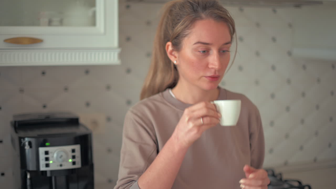 Donna che beve un espresso vicino a una macchina da caffè in una cucina