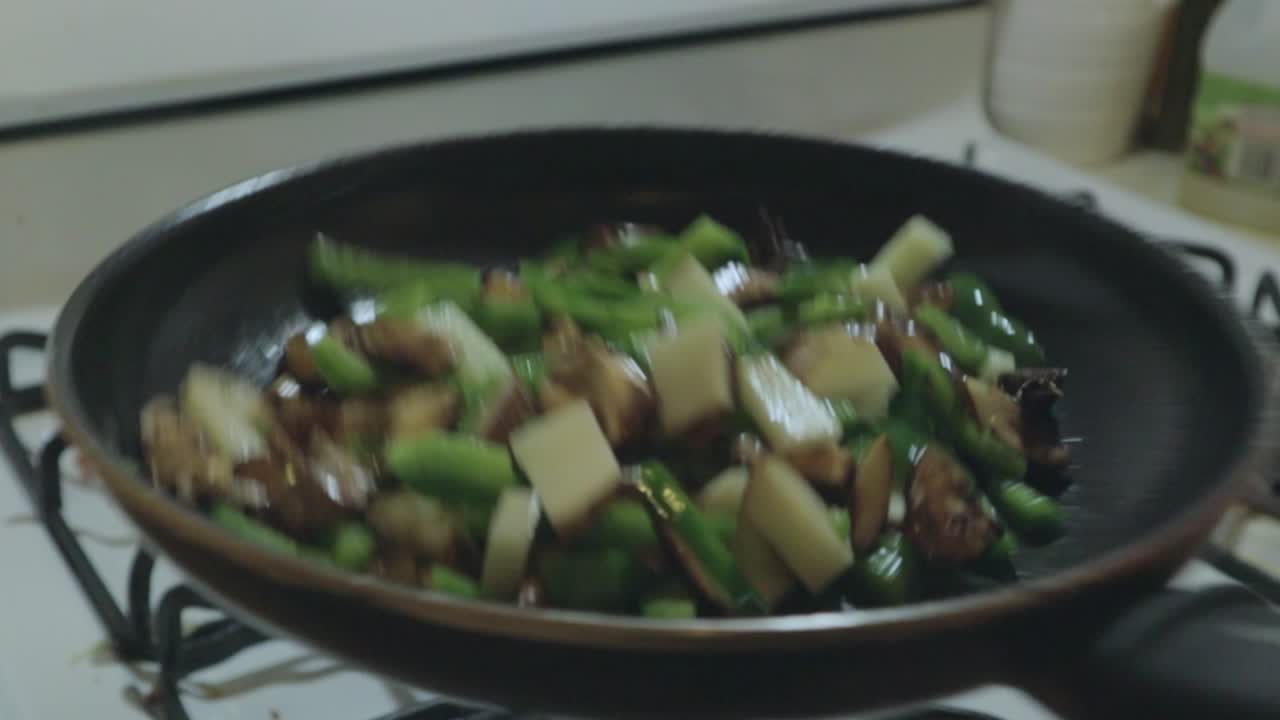 Shaking vegetables drizzled in olive oil on a hot pan over the stove
