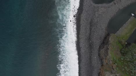 Aerial-view-of-waves-crushing-into-a-pebble-beach,-turquoise-water-and-white-foam