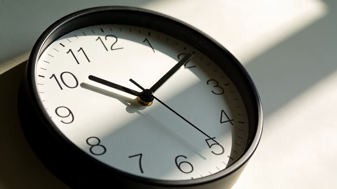 Driven by sunlight through blinds, ticking round analog clock showing seconds passing on white dial