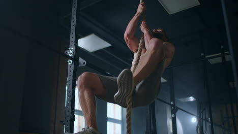 un hombre fuerte en el gimnasio sube por la cuerda y llega a la cima