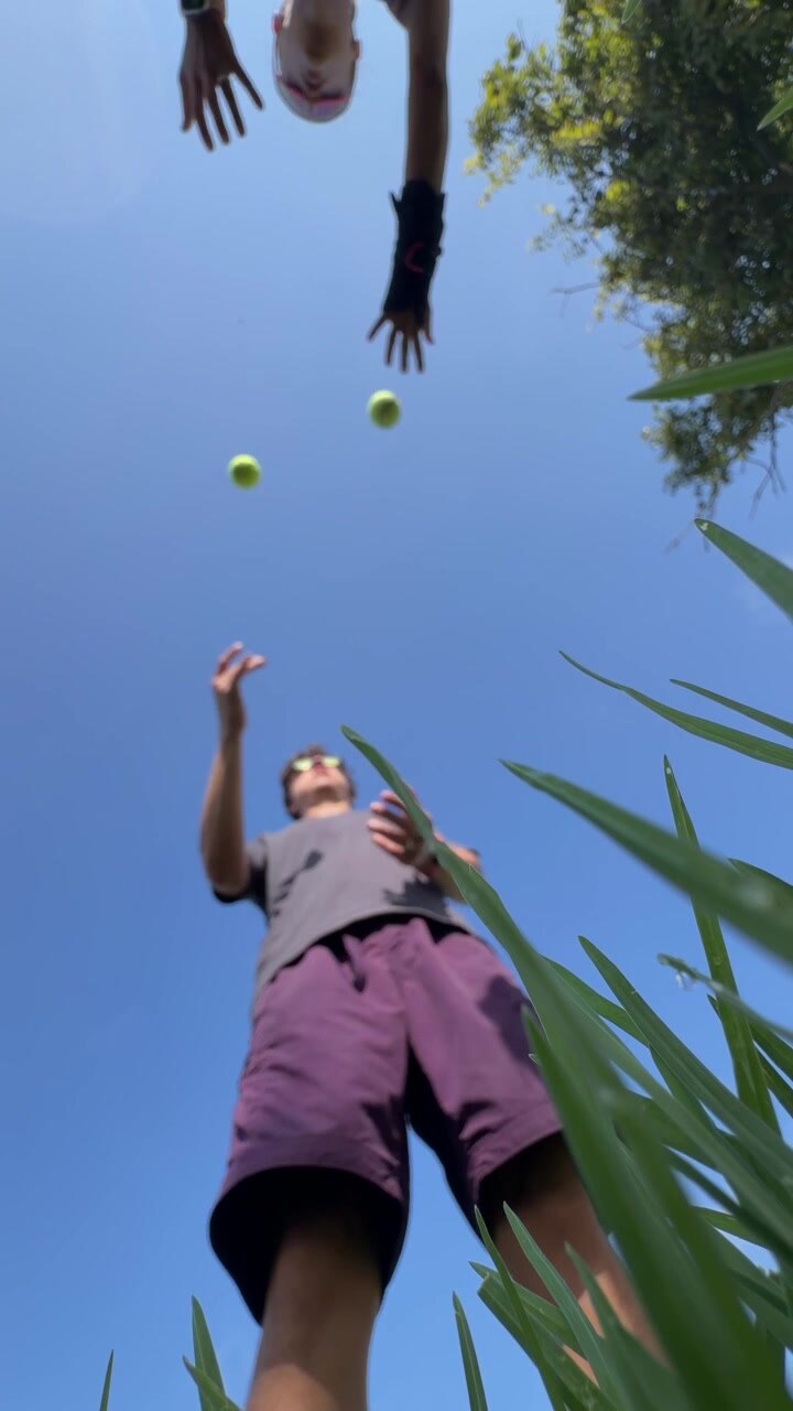 Young Man Juggling Tennis Balls Outdoors Under Clear Blue Sky