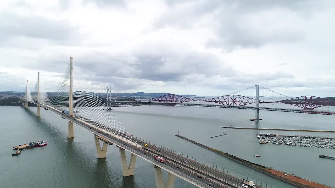 Rising drone footage showing Queensferry Crossing, Forth Bridge and Forth rail Bridge on calm cloudy day.