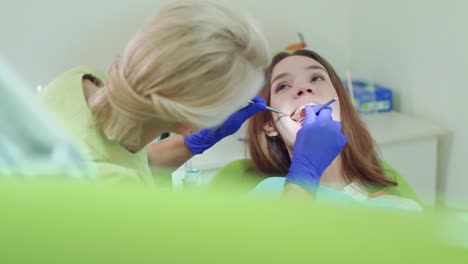 Dental-technician-examining-patient-teeth-with-dental-instruments