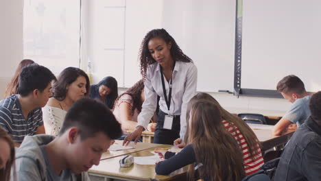 female high school teacher talking to student sitting at desks during lesson