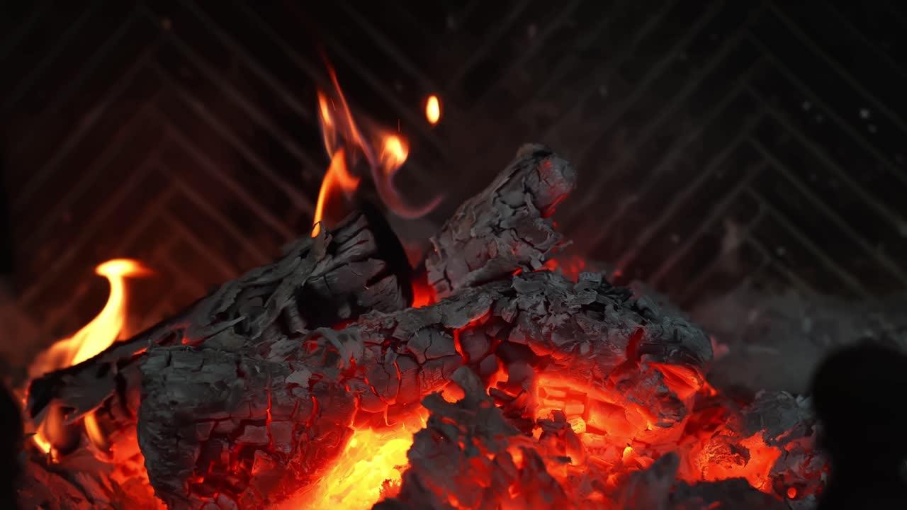 Makrobillede af glødende stykker træ og en forkullet træstamme i en pejs, flakkende flammer over varme kul for hyggelig vintervarme og en filmisk stemning