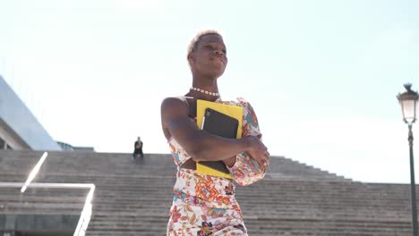 confident black lgbtq woman with notebooks walking on street