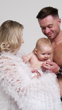 caucasian family having little baby. man with bare torso and blonde woman in white blouse with their son in studio. white backdrop. vertical video