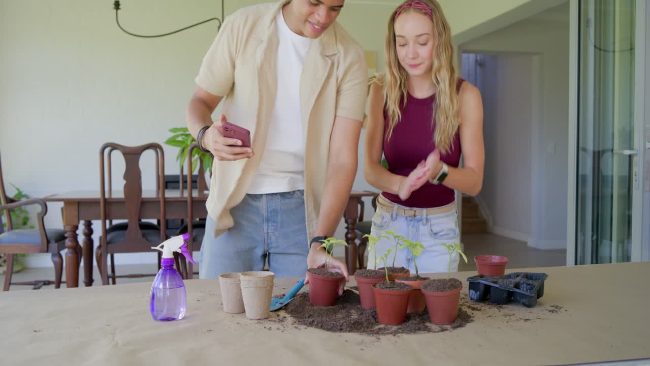 Casal diverso posando para o telefone, depois plantando mudas em uma mesa com terra e uma pá de jardinagem para conteúdo.