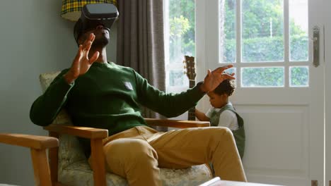 vista frontal de un joven padre negro usando auriculares de realidad virtual en un cómodo hogar 4k