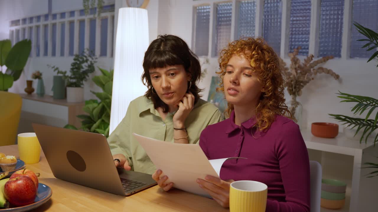 Two women discussing documents while using a laptop
