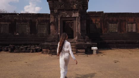 young beautiful woman in long white dress going to palace in wat phou – ruined khmer hindu temple complex. champassak, laos, asia. sunny day. ancient culture religious architecture, ruins. slow motion