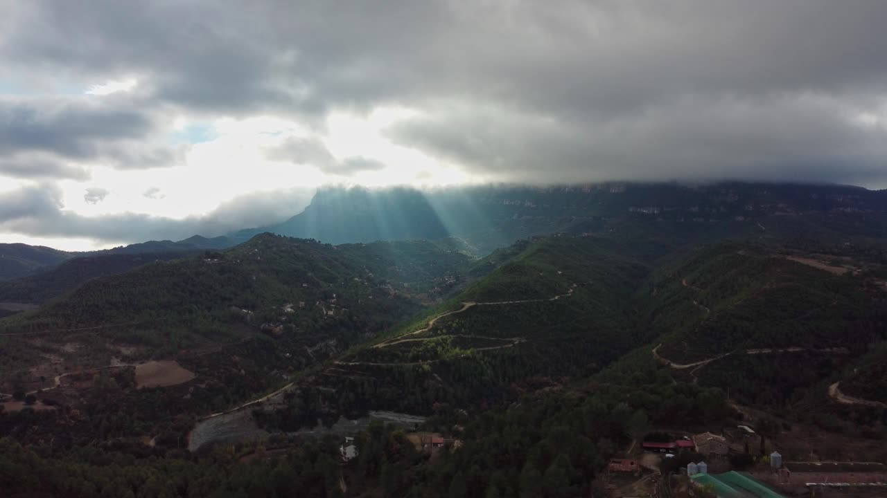 la luz del sol rompiendo a través de las nubes sobre las montañas de montserrat y marganell
