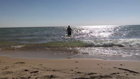 caucasian middle aged male walking in swimsuit into lake michigan water on the beach