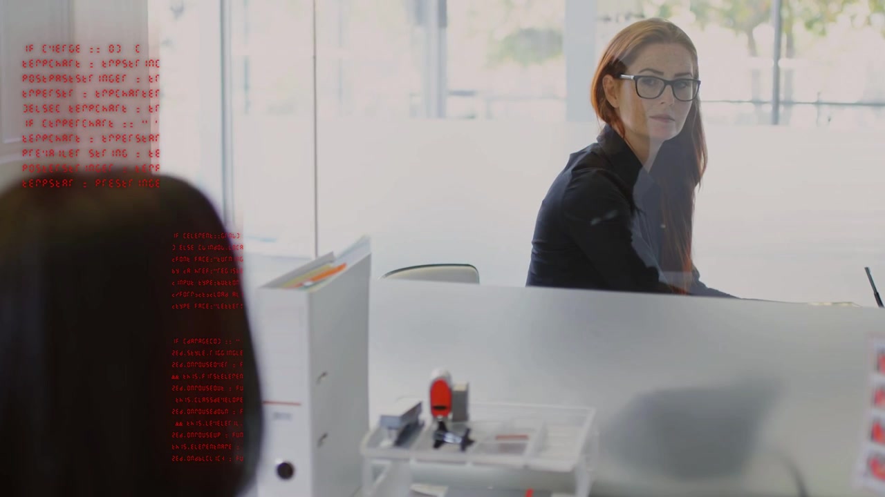 Frau mit Brille wendet sich nach einem Anruf an einen Kollegen und antwortet mit einer roten Code-Überlagerung auf einer gläsernen Technologie.