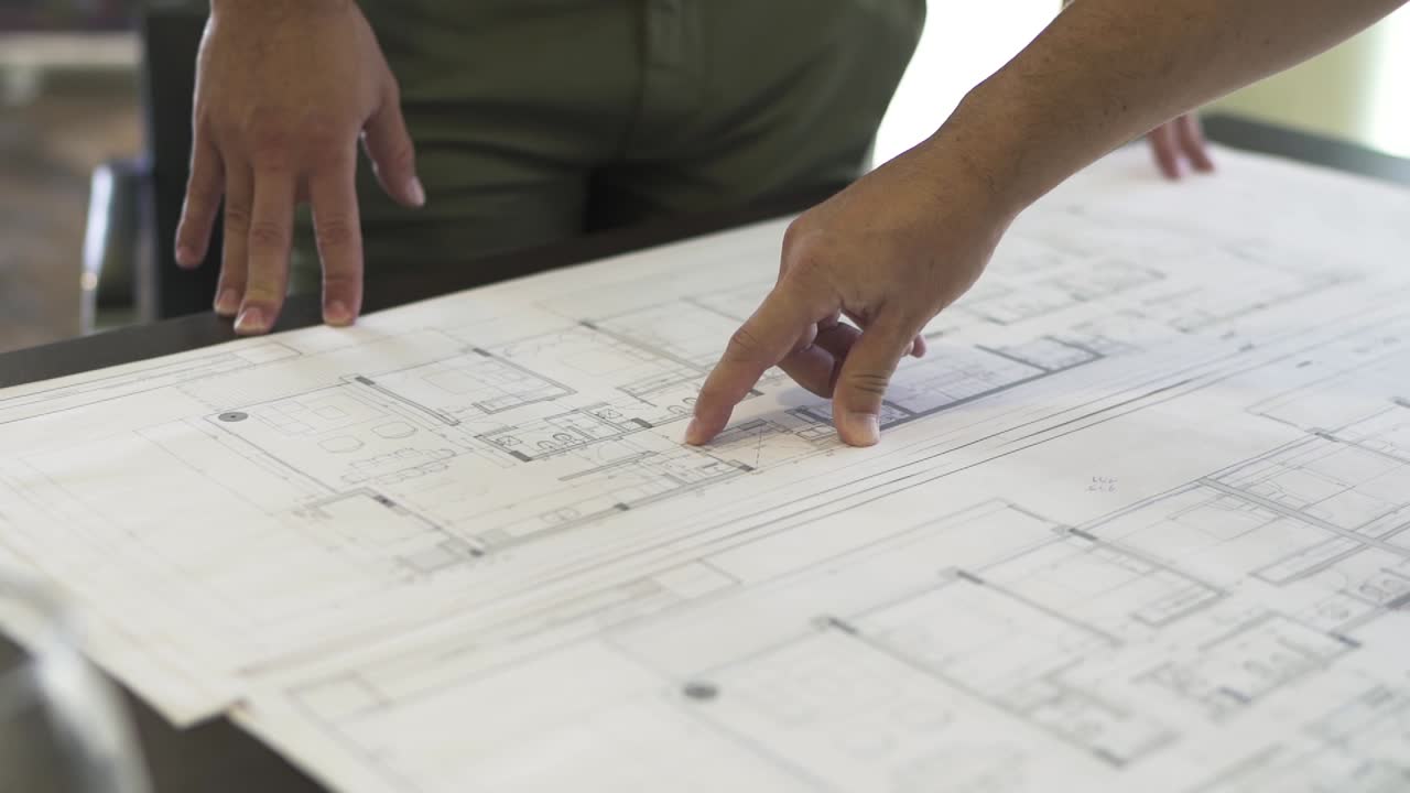 un arquitecto detalla el intrincado plan de una casa, su dedo guiando a través de cada esquina y curva