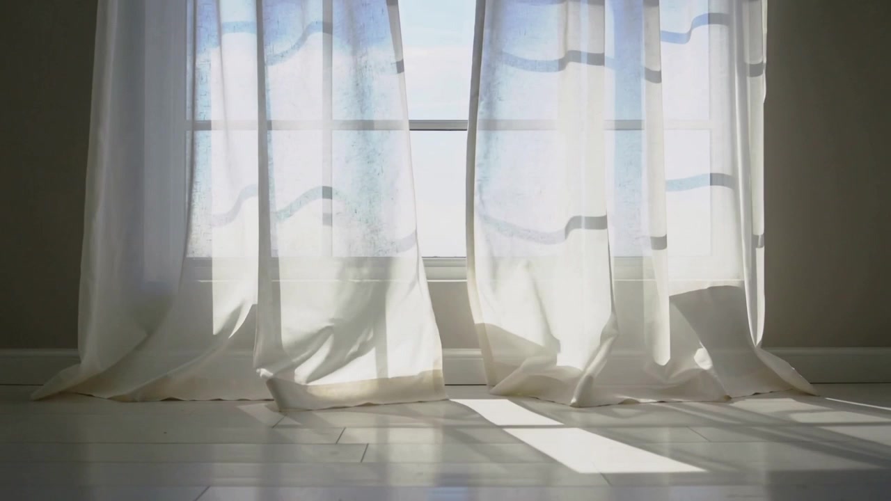 Swaying sheer curtains lifting from paned window at home by gentle breeze, shifting sunlight patch
