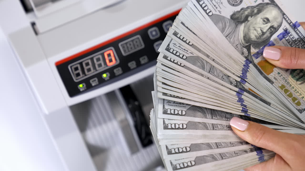 Woman holding money near counting machine at table indoors, closeup