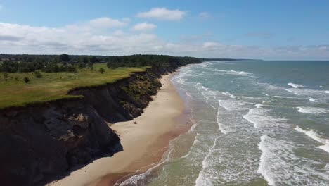 flying over coastline baltic sea ulmale seashore bluffs near pavilosta latvia and landslides with an overgrown, rippling cave dotted cliff and pebbles