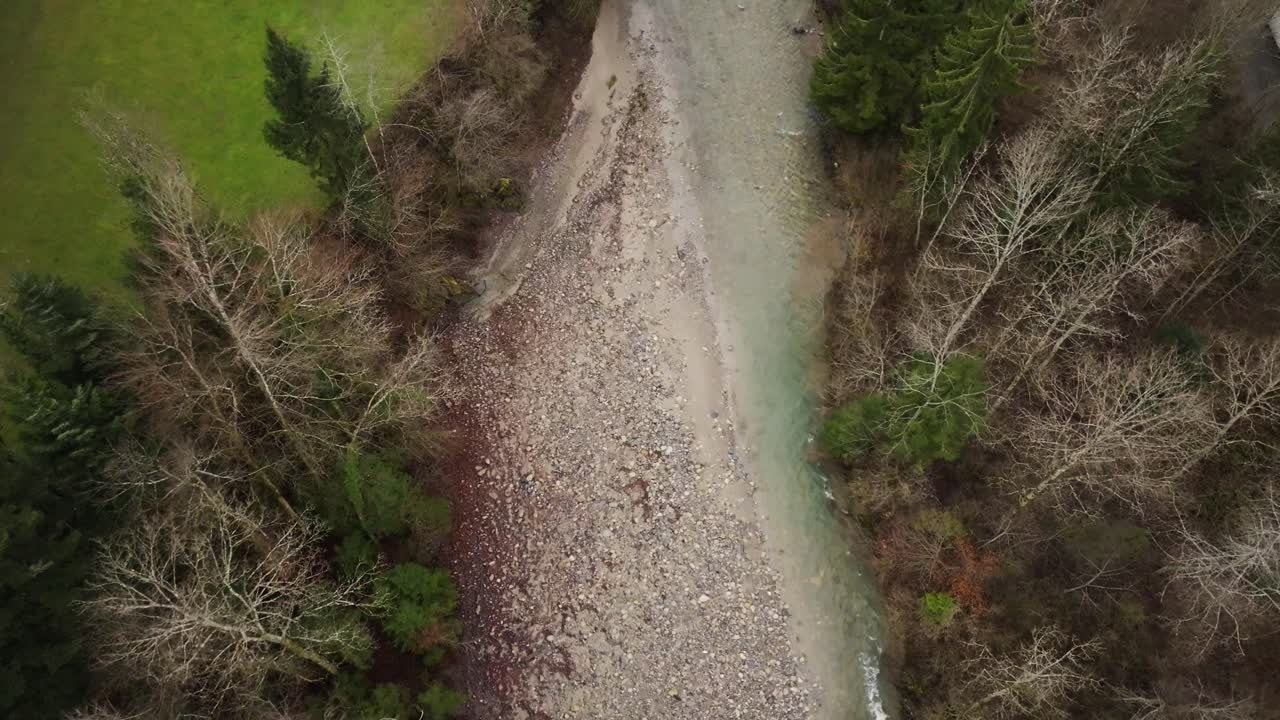 Aerial view of a rocky riverbed with clear water flowing through a forest. Trees line both sides, creating a peaceful natural landscape ideal for ecology, environment, and nature themes