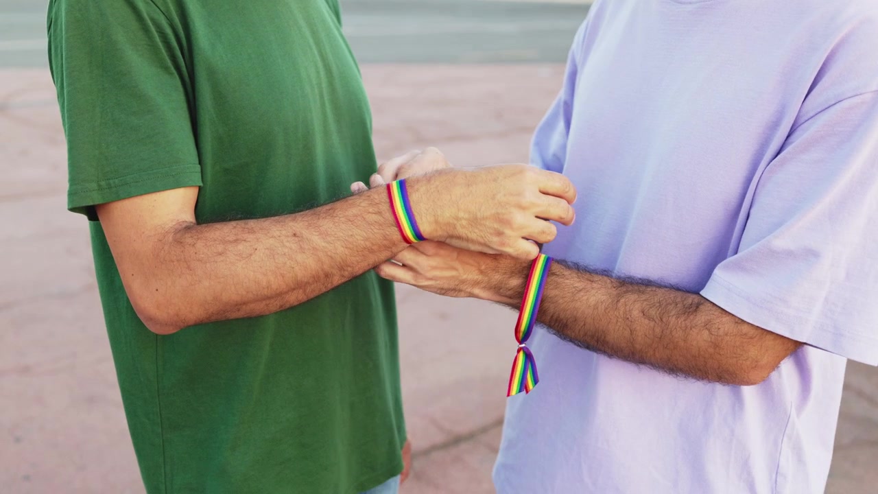 Henkilö sitoo sateenkaari-pride-rannekorua toisen ranteeseen