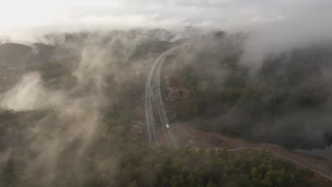 Imágenes-De-Drones-De-La-Carretera-Y-La-Urbanización-En-Noruega-Con-Algo-De-Niebla-Flotando-En-El-Aire-Y-El-Sol-Iluminando-Las-Nubes
