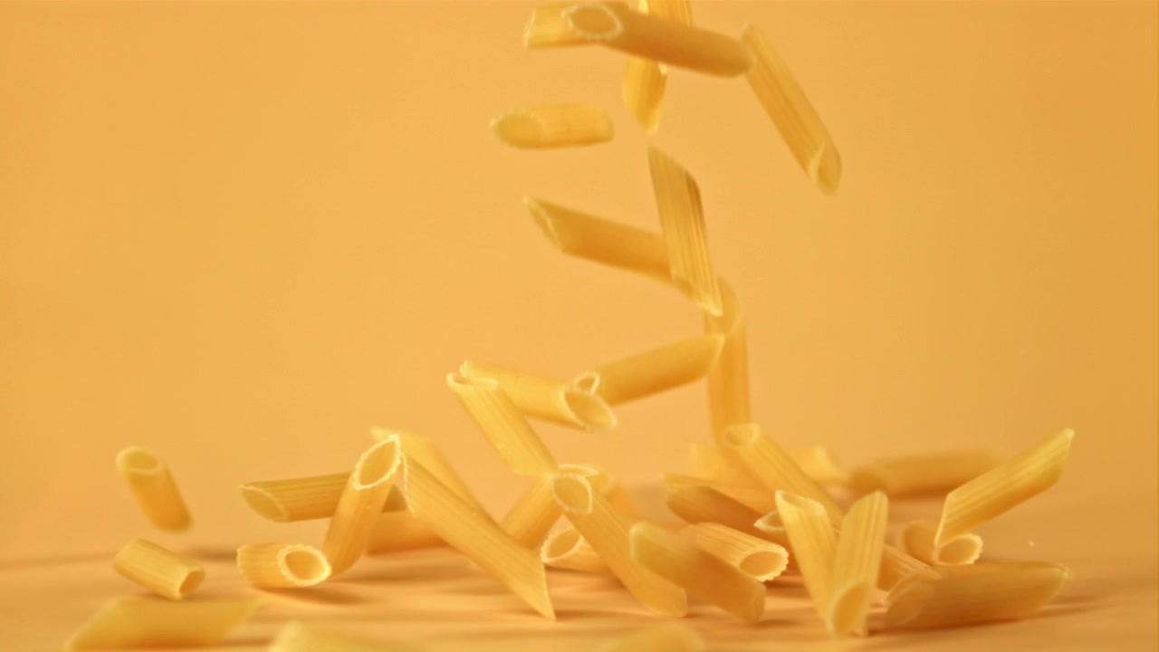 Pasta penne che cade al rallentatore su uno sfondo giallo