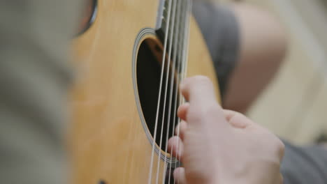 cerrar imágenes en cámara lenta de los dedos de un hombre tocando una guitarra acústica en un estudio