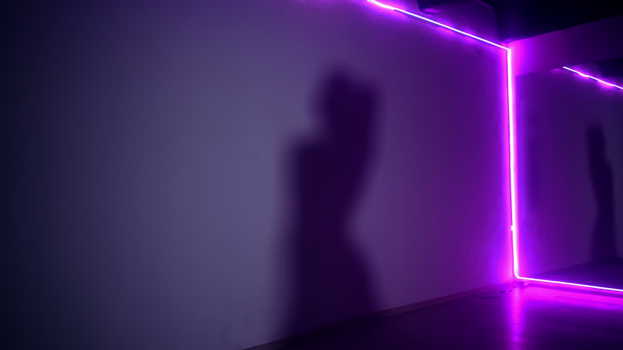 Shadow of a long-haired woman moving on the wall. Female figure dancing in the room with purple light.