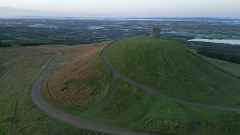 Stone-squat-tower-on-hilltop-at-dawn-with-orbit-revealing-lowland-countryside-in-autumn